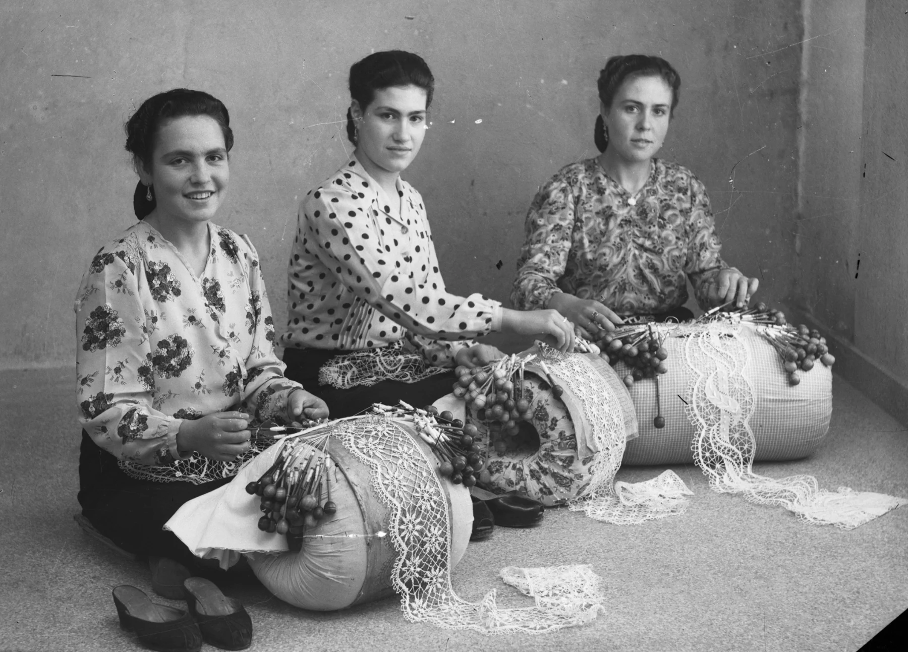 Fotografia de arquivo de três rendilheiras com almofadas e bilros