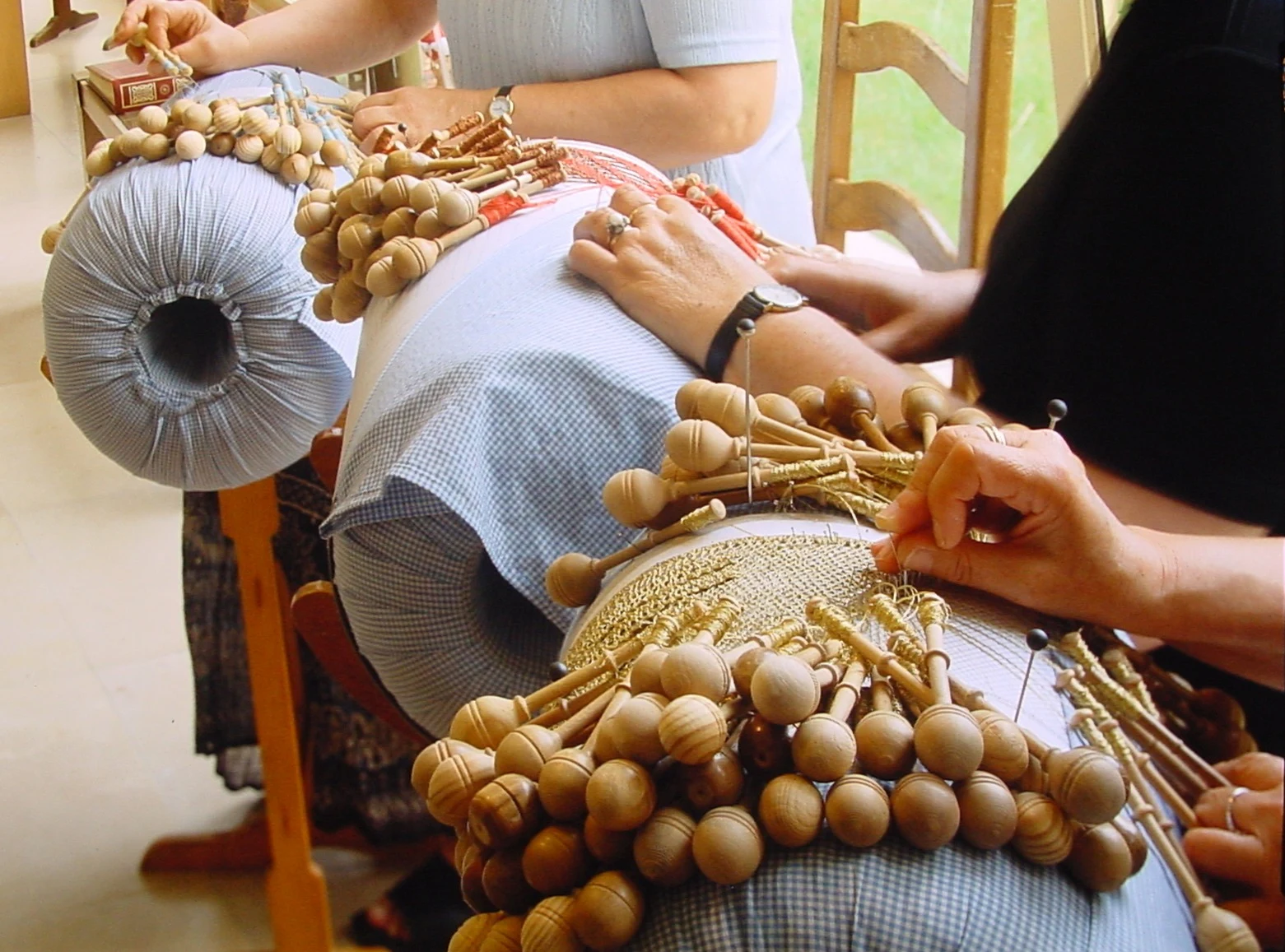 Mãos de uma rendilheira a trabalhar com bilros numa almofada
