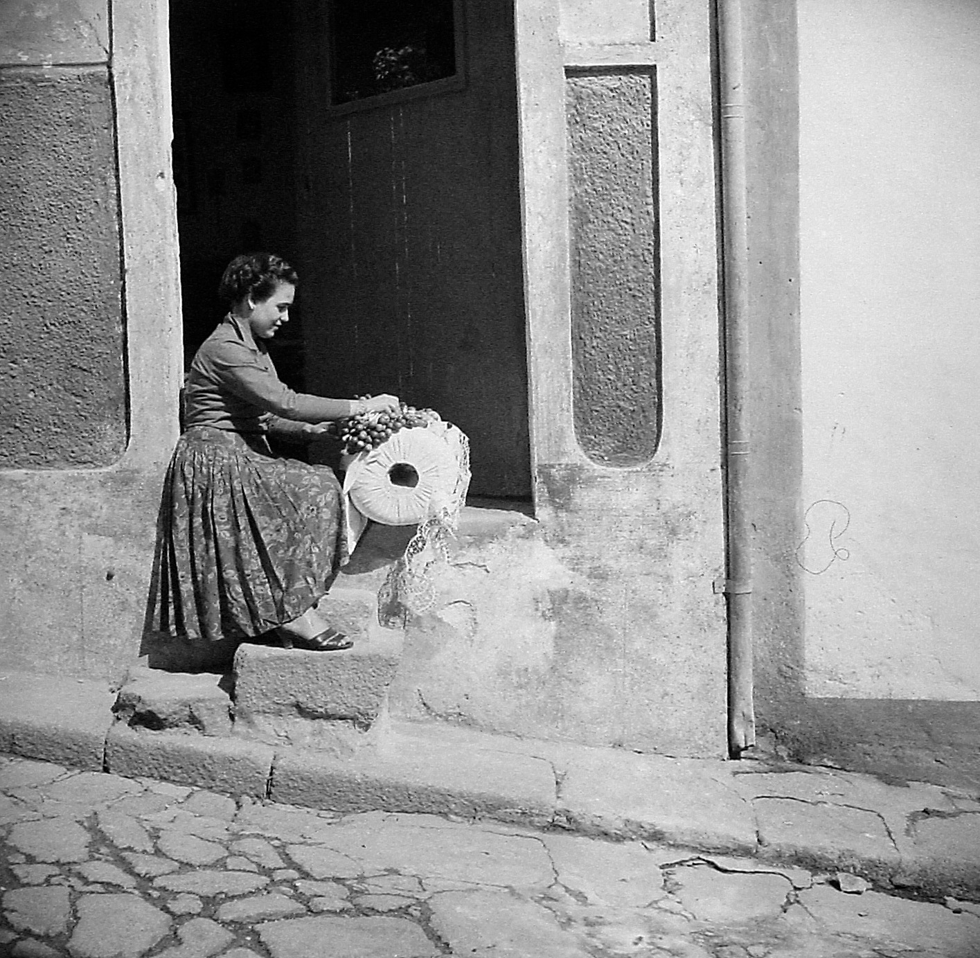 Fotografia histórica de uma rendilheira a trabalhar à porta de uma casa
