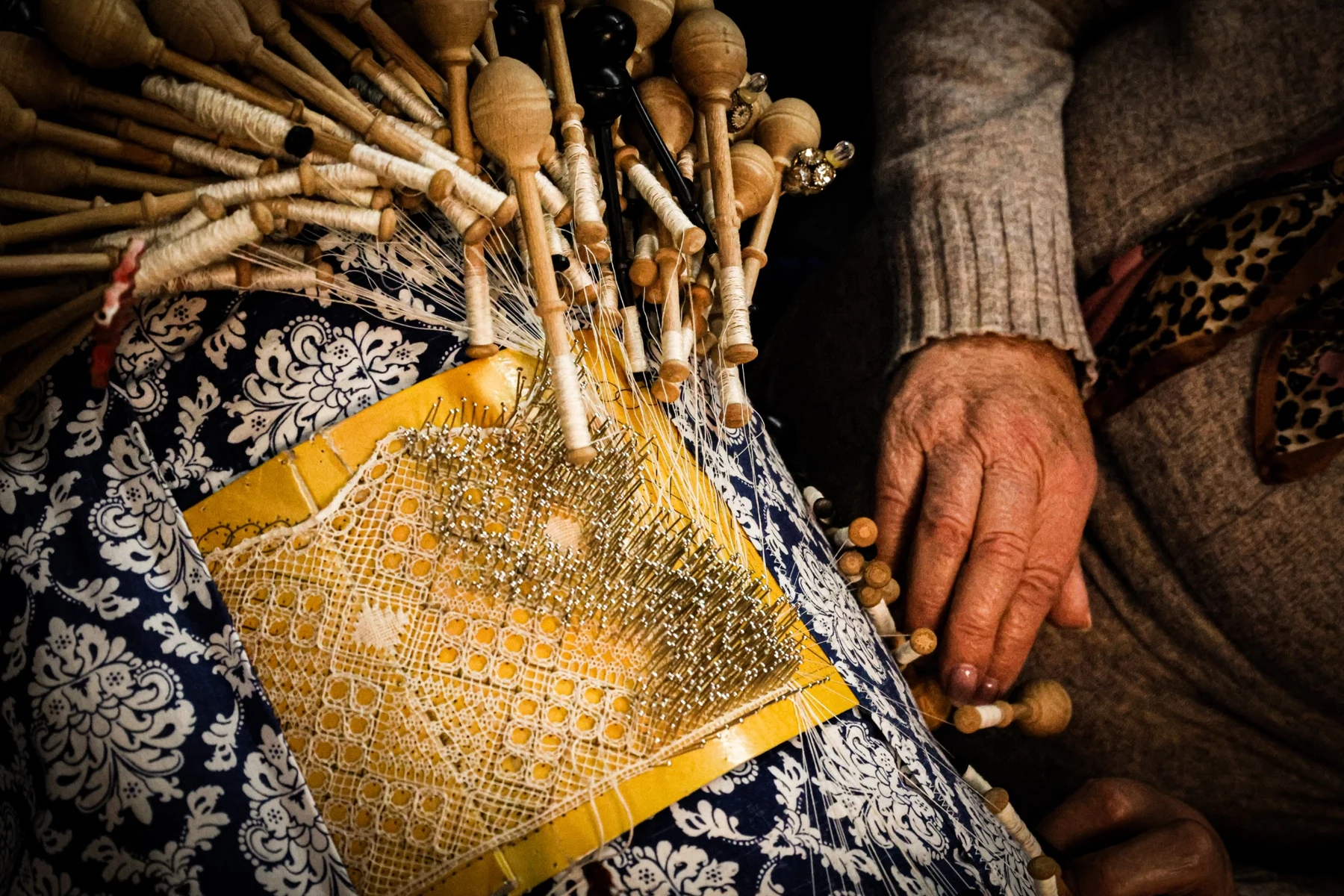 Bilros de madeira e renda em execução nas mãos de uma rendilheira